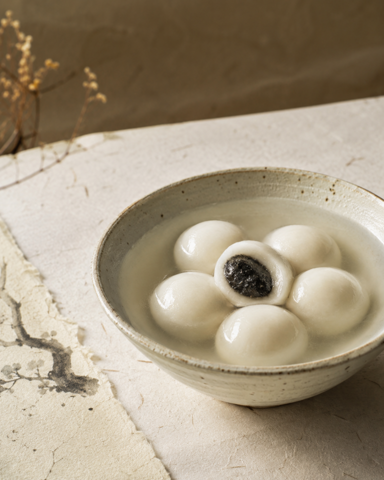 White tangyuan in a ceramic bowl, with one dumpling opened to show a dark filling